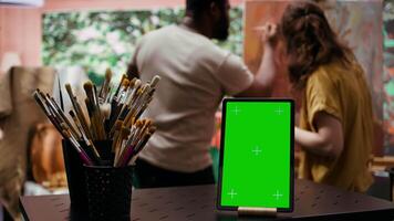 In a creative atelier, painters use colorful paint tubes and brushes to create a masterpiece next to copy space display. Team of artists working on a nature inspired painting. Camera B. video