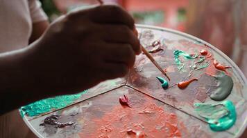Talented artist using modern tools and painting supplies to create an artwork, mixing watercolors on a palette during his creative process. Man working on a masterpiece. Close up. Camera B. video