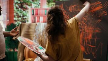Talented artist and her apprentice engage in finger painting hobby in art and craft workshop, using modern painting technique to create abstract masterpiece. Vibrant colors on the canvas. Camera A. video