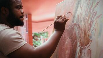 Male artist painting a modern artwork with watercolor and palette, working on his new creation in art and craft workshop. Young painter creating a rustic masterpiece on canvas. Camera B. video
