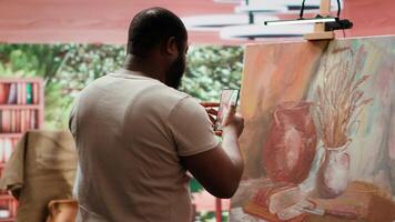 Skilled painter recording a of his finished creation for self promotion, using his online presence for digital marketing and fame. Feeling proud of his new artwork content creation. Camera A. video