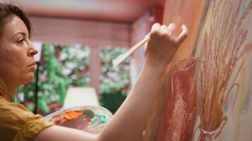 Female painter working on a canvas to create an artwork in studio, using bristles to apply dye with precision. Presenting her skill to create unique painting for the art gallery. Camera B. video