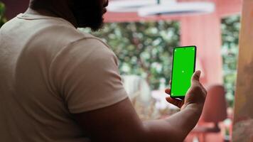 Young artist looking at isolated chroma key display in his painting atelier, using device next to canvas with colorful masterpiece. Painter creating rustic artwork for gallery exhibition. Camera A. video