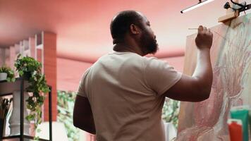 African american artist using his skill to paint a new creation in art studio, using innovative painting technique for his masterpiece. Young contemporary painter working on an artwork. Camera A. video