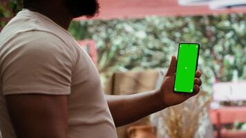 African american artist holding device with green screen mockup in art studio, working on a new painting with a certain technique. Painter using watercolor and acrylic dye for his creation. Camera A. video
