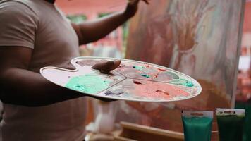 Confident painter mixing different watercolors on palette to create the perfect shade and apply on canvas, on fine art. Artist uses vibrant colors and dynamic brushwork. Close up. Camera B. video