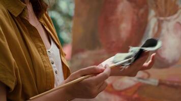 Female painter wiping off paint from paintbrush before mixing different colors, creating rustic masterpiece with paint tubes. Artist showing her skill and creativity in atelier. Close up. Camera A. video