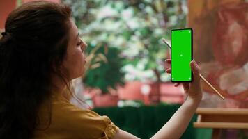 Young woman looking at chroma key display and at her rustic masterpiece, feeling proud and confident with her paintwork for the art gallery. Artist enjoying her hobby for leisure. Camera A. video
