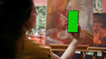 Young woman looking at chroma key display and at her rustic masterpiece, feeling proud and confident with her paintwork for the art gallery. Artist enjoying her hobby for leisure. Camera B. video