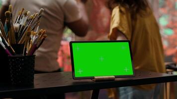 Two artists painting on a canvas next to green screen on tablet display, working together on their new masterpiece for fine art gallery exhibition. Diverse team of painters in art studio. Camera A. video