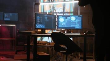 Hacker arrives in messy base of operations with neon lights and graffiti drawings sprayed on walls. Cybercriminal using ghetto hideout as HQ to commit illegal activities using computer, camera A video