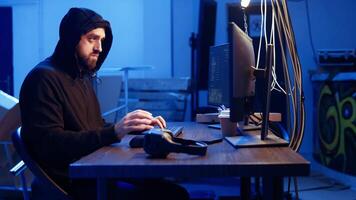 Hacker listens music while hiding in underground bunker and coding, stealing data from victims using PC virus. Rogue programmer wearing headphones tricks people into installing ransomware, camera A video