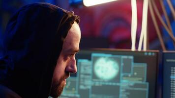 Hooded hacker targeting vulnerable unpatched connections, seeking to compromise digital devices and steal valuable sensitive data. Evil man running code in graffiti painted basement, camera B close up video