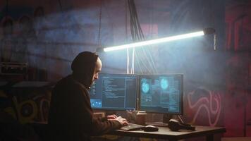 Hacker in foggy neon illuminated basement with graffiti drawings on walls using advanced technology computer, running code. Cybercriminal using dark underground warehouse as crime haven, camera B video
