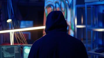 Tracking shot of hooded spy in underground hideout stealing valuable data by targeting governmental websites with weak security. Espionage specialist using tablet to launch cyber attacks video