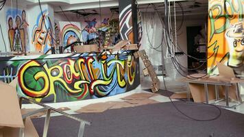 Electric cables hanging in empty dirty criminals headquarters with graffiti drawings sprayed on walls. Derelict ghetto hideout used by vandals to commit illegal activities, handheld camera shot video