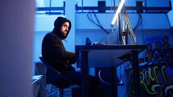 hacker dentro escondido abrigo ouvindo música enquanto lançamento ddos ataques em sites, falhando eles de enviando ampla tráfego. homem vestindo fones de ouvido implantando vírus em vítimas computadores, Câmera uma video