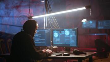 Hacker using high tech computer system to run malicious code in foggy dark basement. Rogue programmer committing illegal activities using PC in neon illuminated criminal hideout, camera A video