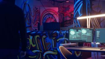 Hacker arriving in underground base, looking at spray cans in industrial warehouse with graffiti drawings. Cybercriminal waiting for hacking process, looking at paint cans in crime haven, camera B video