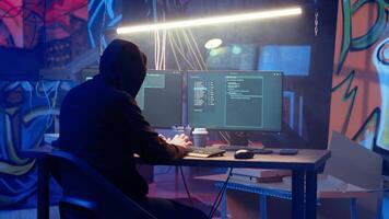 Hooded hacker leaving neon lit underground shelter after launching DDoS attack on websites. Cybercriminal finishing work on script that can crash businesses servers, exiting headquarters, camera B video