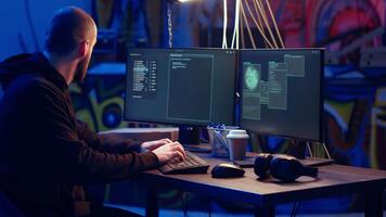 Hacker listens music while hiding in underground bunker and coding, stealing data from victims using PC virus. Rogue programmer wearing headphones tricks people into installing ransomware, camera B video