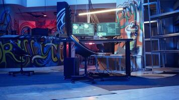 High tech computer system running malicious code in empty basement, handheld camera shot. PC monitors in empty neon lit criminal hideout used by hackers to commit illegal activities, camera A video