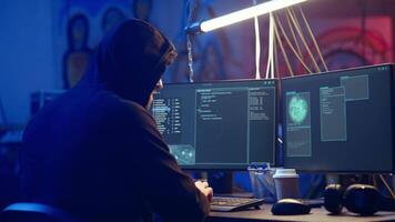 Hooded hacker creating pirating crack for software and game releases in bunker. Rogue programmer getting past anti tamper measures implemented by companies to protect their products, camera A video