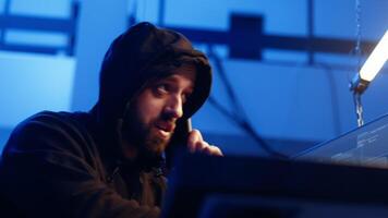 Hacker hiding in underground bunker, chatting with friend in telephone call, anxious after stealing data from victims using computer virus, scared about being caught by police, camera A close up video