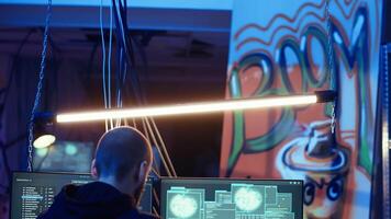 Hacker in hidden shelter listening music while launching DDoS attacks on websites, crashing them by sending large traffic. Man wearing headphones deploying viruses on victims computers, camera B video
