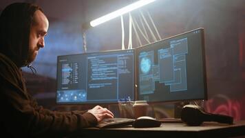Hacker in foggy neon illuminated basement with graffiti drawings on walls using advanced technology computer, running code. Cybercriminal using dark underground warehouse as crime haven, camera A video