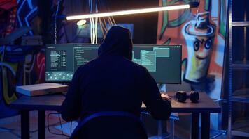 Hooded man in underground hideaway utilizing technical knowhow of bugs and exploits to break into computer systems and access valuable data, bypassing firewalls and login process, dolly in shot video