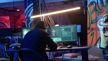 Skilled hacker deploying malware on unaware victims computers, stealing sensitive and private information, selling on darknet to highest bidder, looking at computer screen in hideout, camera A video