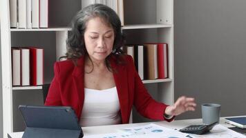 Senior woman accountant calculations and analyzing financial graph data with calculator and laptop Business video