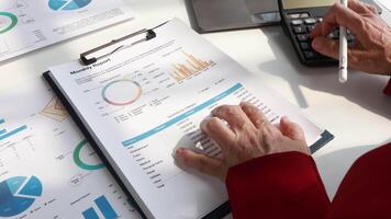 Close-up of senior auditor's hand counting expenses of company employees using calculator and cashier's checks to prepare financial report on costs for manager sits at table in office video