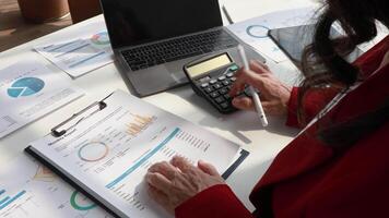 Senior woman accountant calculations and analyzing financial graph data with calculator and laptop Business video
