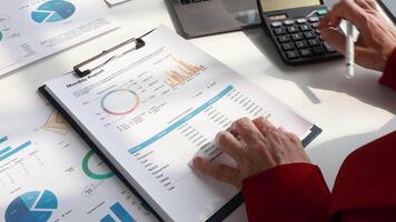 Close-up of senior auditor's hand counting expenses of company employees using calculator and cashier's checks to prepare financial report on costs for manager sits at table in office video