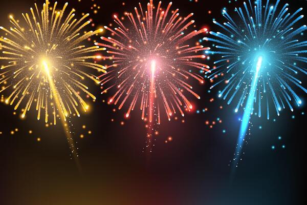 Bright red, blue, and yellow fireworks burst in a dark night sky