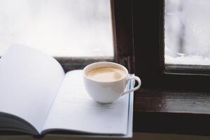 Cozy winter day with steaming coffee, open book, and candlelight by the snowy window photo
