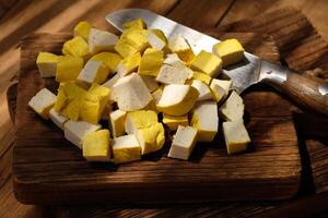 sliced yellow tofu on a teak wood cutting board. stainless steel blade. soy bean products. photo