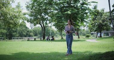 Handheld shot, Cheerful woman is walking in a park on a sunny day, surrounded by lush green trees, and enjoys taking pictures of the nature with her camera. A relaxing weekend moment. video