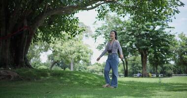 Handheld shot, Cheerful woman is walking in a park on a sunny day, surrounded by lush green trees, and enjoys taking pictures of the nature with her camera. A relaxing weekend moment. video