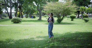 Handheld shot, Cheerful woman is walking in a park on a sunny day, surrounded by lush green trees, and enjoys taking pictures of the nature with her camera. A relaxing weekend moment. video