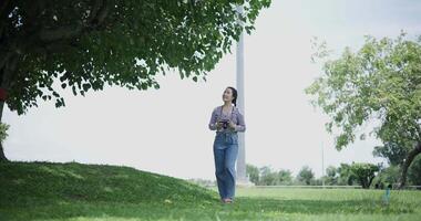 Handheld shot, Cheerful woman is walking in a park on a sunny day, surrounded by lush green trees, and enjoys taking pictures of the nature with her camera. A relaxing weekend moment. video