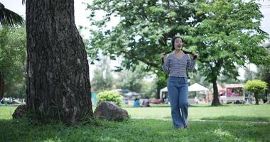 Handheld shot, Cheerful woman wearing headphones is walking in a park, enjoying music surrounded by nature. feeling relaxed and carefree. video