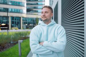 Young happy Caucasian hipster 30s guy standing at metal wall background. Smiling cool stylish trendy gen z teenage student model posing for authentic portrait outdoors. photo