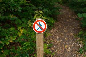 A round sign prohibiting entry into the forest. Shows a crossed-out person. The sign is in focus on the centre of the frame, and the blurred background is a forest green. Ojcowski park photo