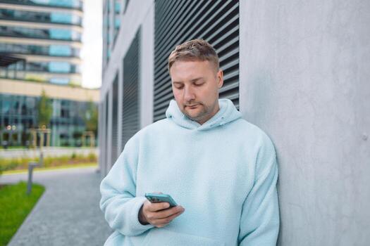 Successful young Caucasian man walking outside office building, engineer software developer programmer smiling and happy using test app on phone photo