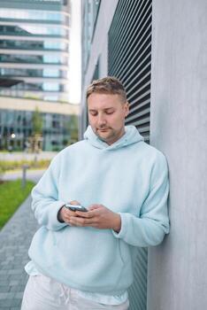 Successful young Caucasian man walking outside office building, engineer software developer programmer smiling and happy using test app on phone photo