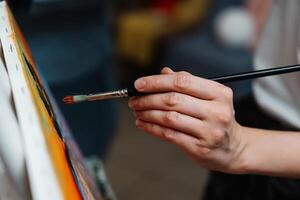 A close-up of an artists hand painting on canvas with a brush in a studio photo