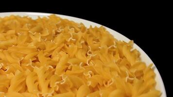 Uncooked Fusilli Pasta on White Plate Rotating against Black Background. Fat and Unhealthy Food. Dry Spiral Macaroni. Italian Culture and Cuisine. Raw Golden Pasta video